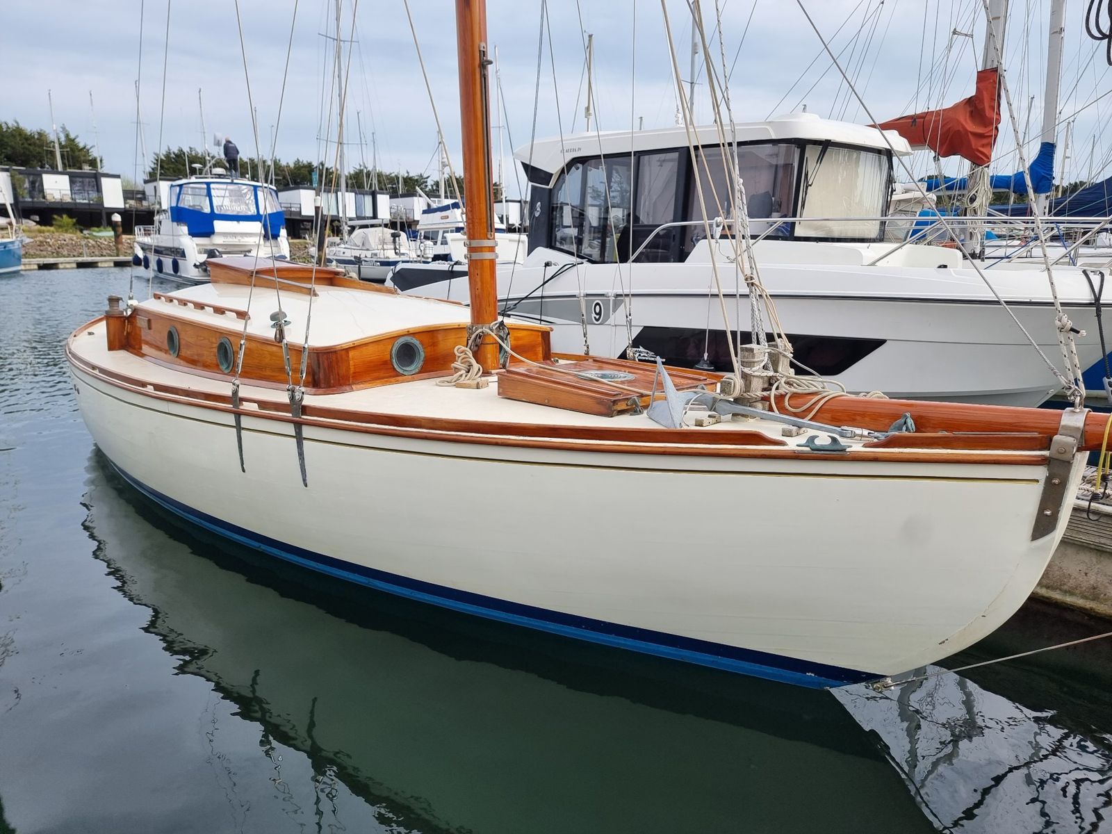 Classic wooden yacht afloat in a marina with cream topsides and freshly varnished coachroof, mast and trim
