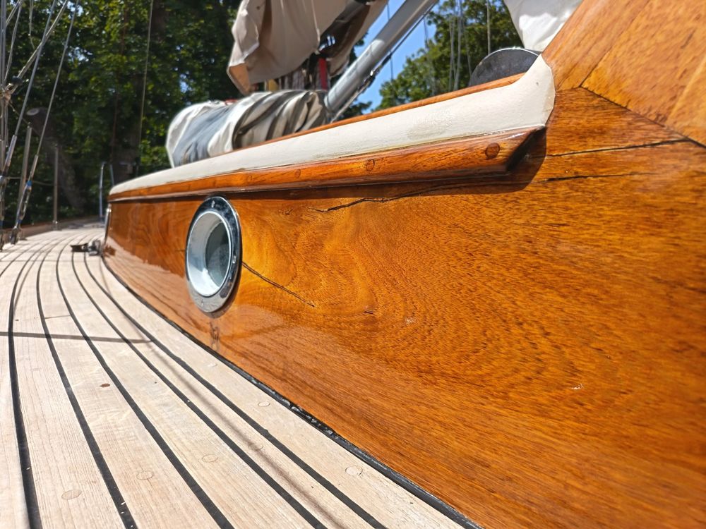 Close view along a gleaming varnished coachroof side above a laid deck