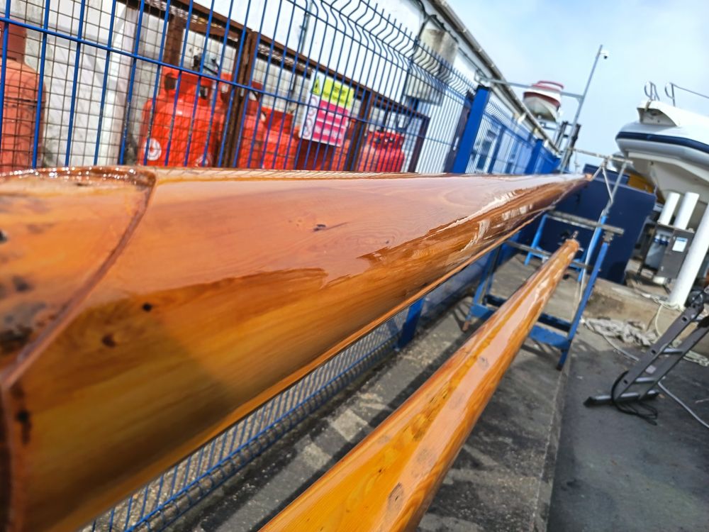 Two wooden spars freshly varnished on trestles in the yard