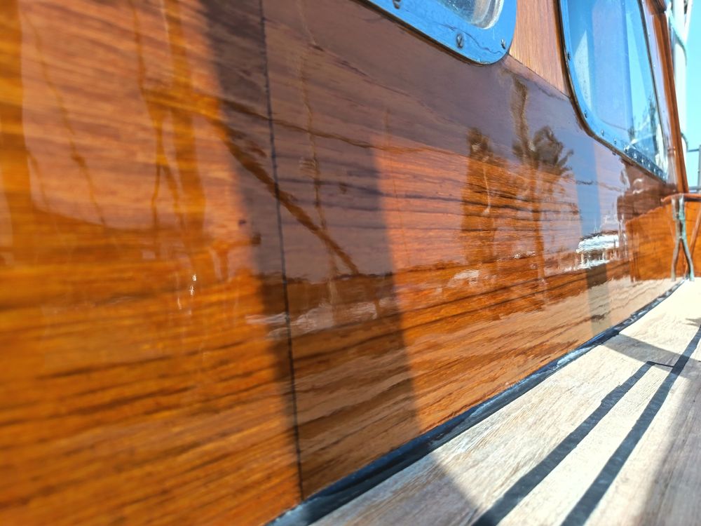Deep gloss varnish on a wheelhouse side reflecting the harbour