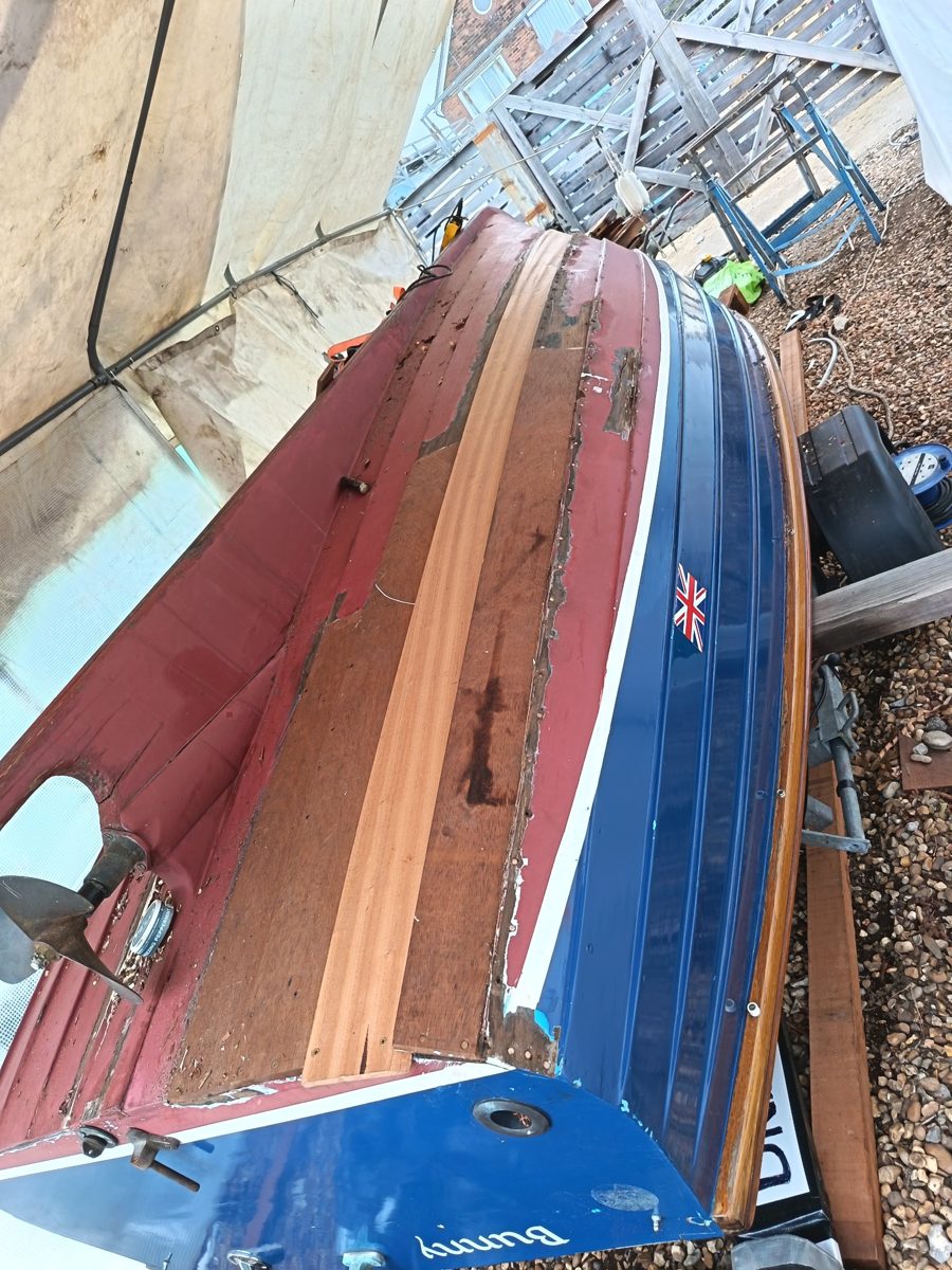 Bunny upturned under cover, with a new pale plank fitted among the old strakes near the transom