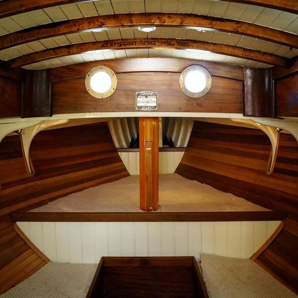 Forward cabin with varnished deck beams, brass portholes and the original tonnage plaque