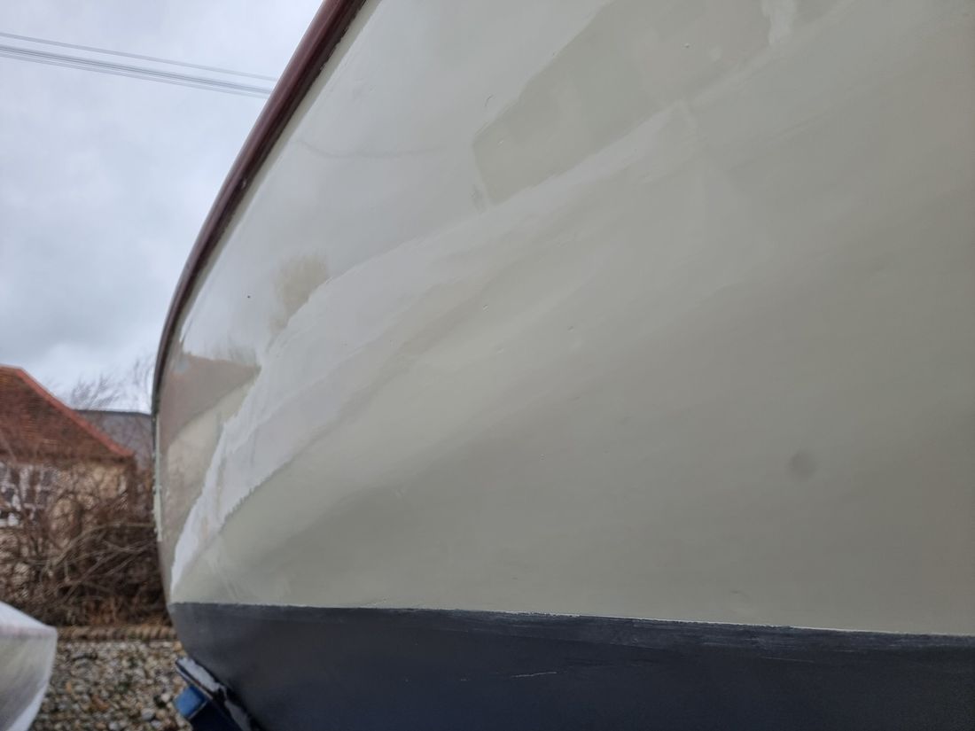 Folkdance's cream topsides faired and repainted to a gloss beneath the varnished toerail