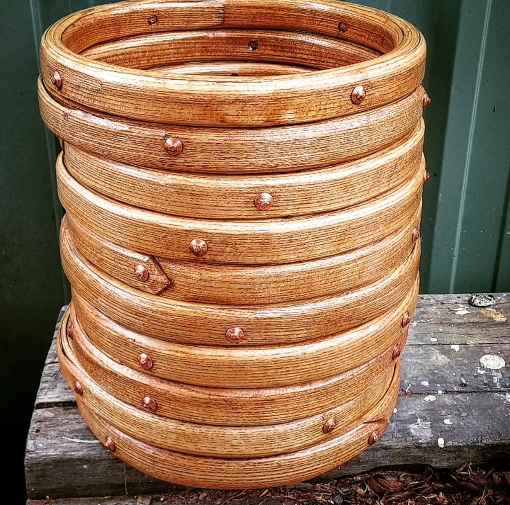 A stack of new steamed ash mast hoops with copper-riveted scarfs, oiled to a deep golden colour