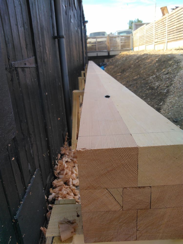 Square mast staves laid up on trestles beside a black timber shed