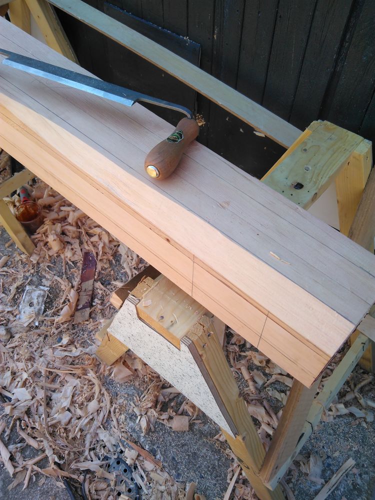 Drawknife resting on a marked-out spar with shavings below