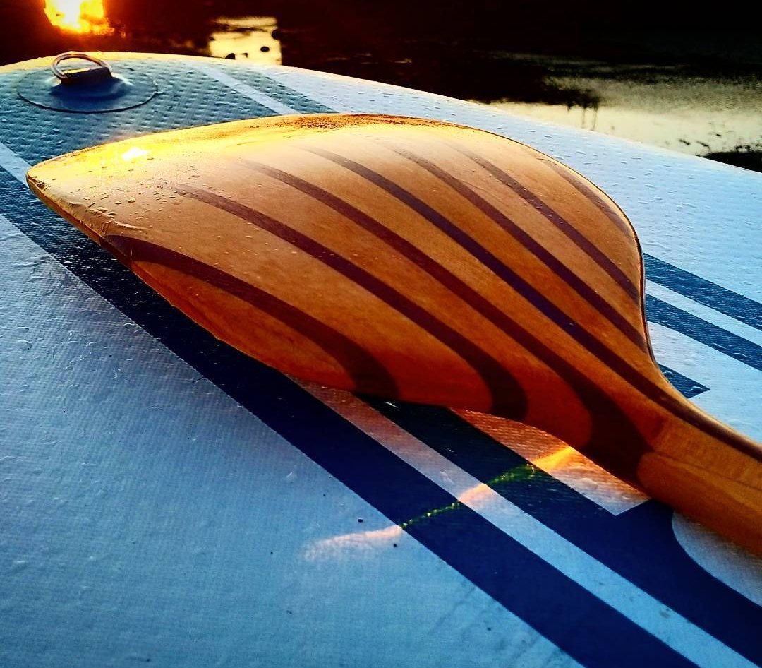 The finished paddle resting on a paddleboard at sunset, water beading on the blade