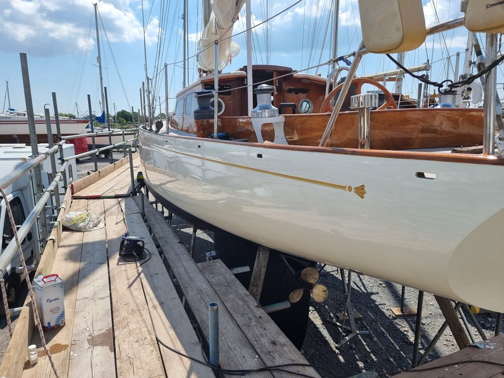Cream topsides with a gilded cove line ending in a carved fan, beneath a varnished cockpit coaming