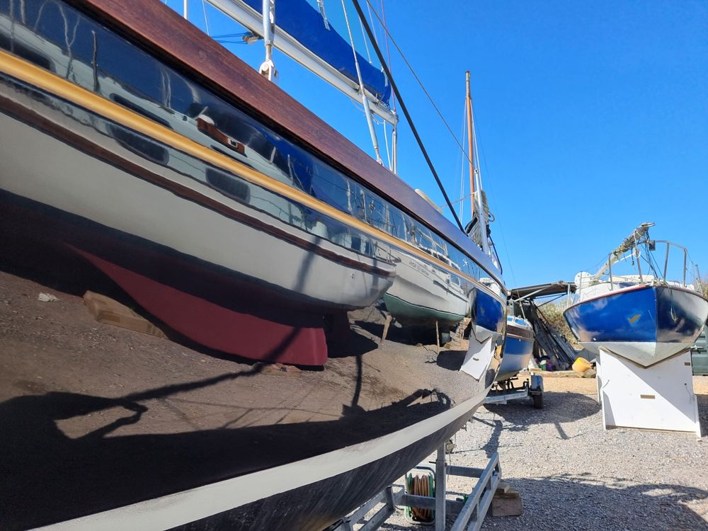 Black Bess's topsides polished to a mirror shine, reflecting the boatyard