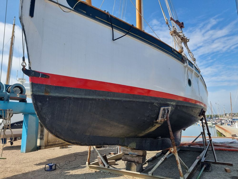 Rhoda in the hoist before repainting, with worn white topsides and a scuffed black bottom