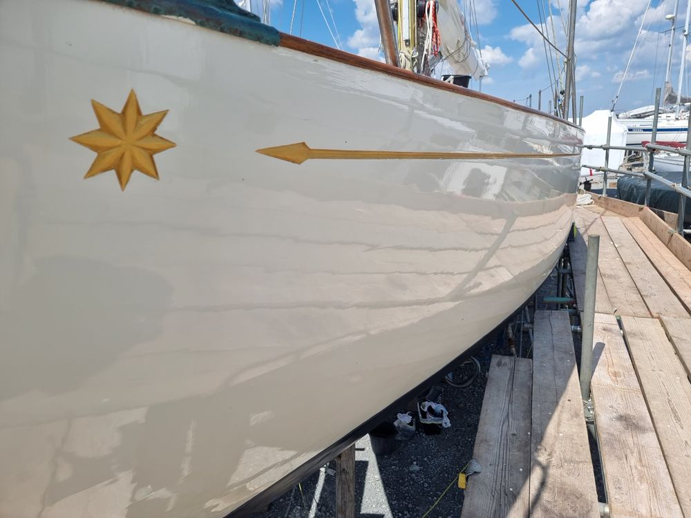 Glossy cream topsides with a gilded eight-point star and arrow-tipped cove line