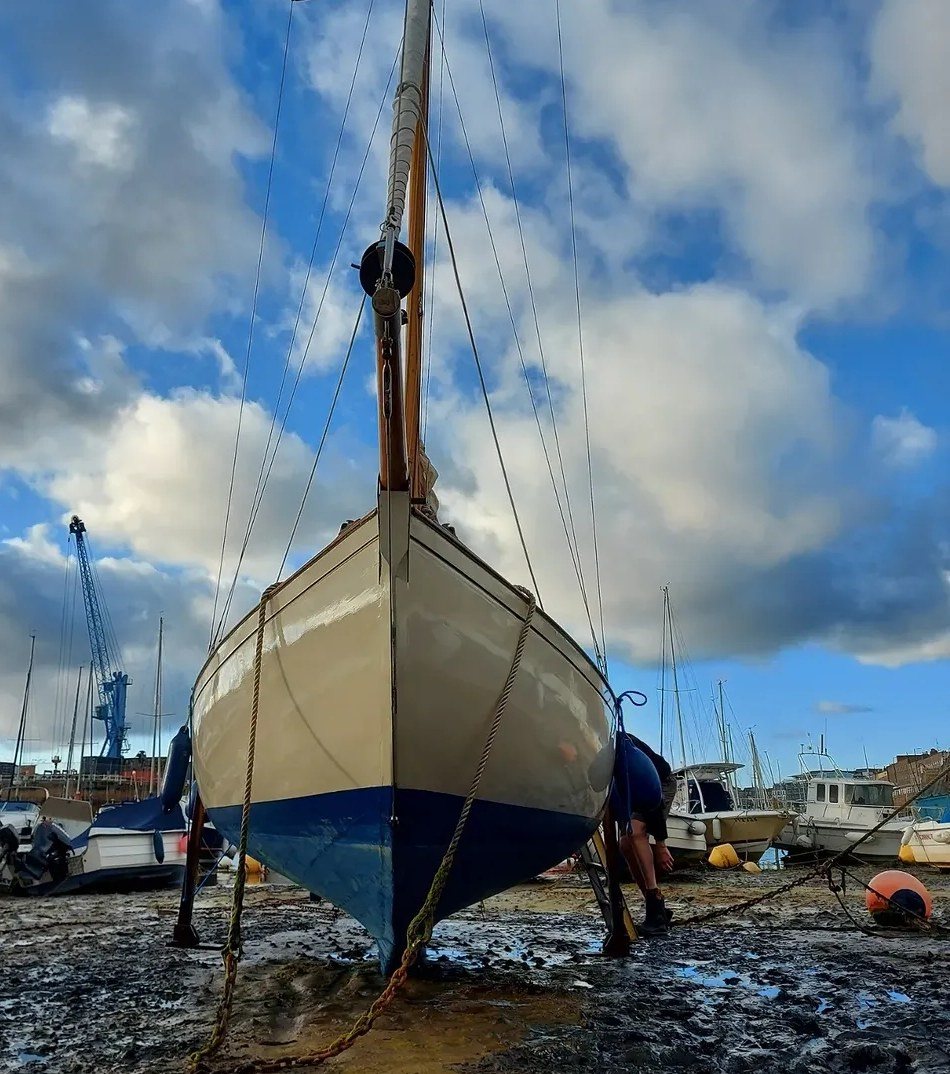 Petrina seen head-on at low tide, her cream topsides and blue bottom paint gleaming