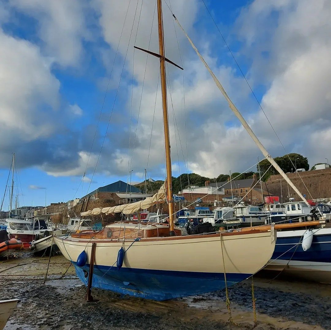 Petrina restored, dried out on the harbour bed in St Helier with cream topsides, blue bottom and varnished mast and coachroof