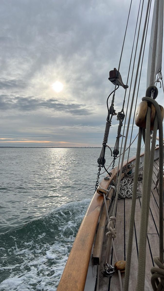 Looking forward along Rhoda's rail at sunset, rigging silhouetted and wake curling away