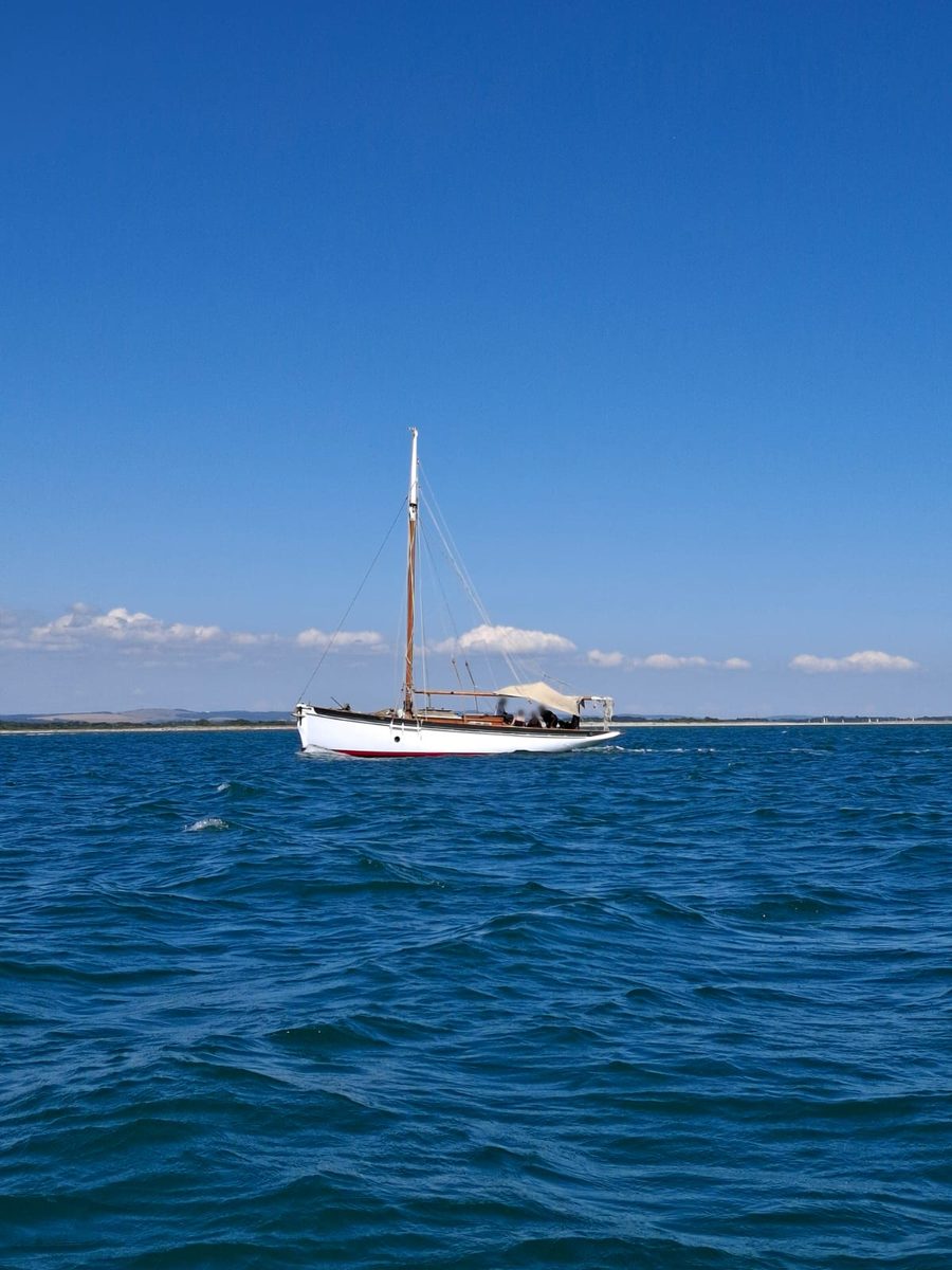 Rhoda under sail on open water beneath a clear blue sky, a cream awning rigged over the cockpit
