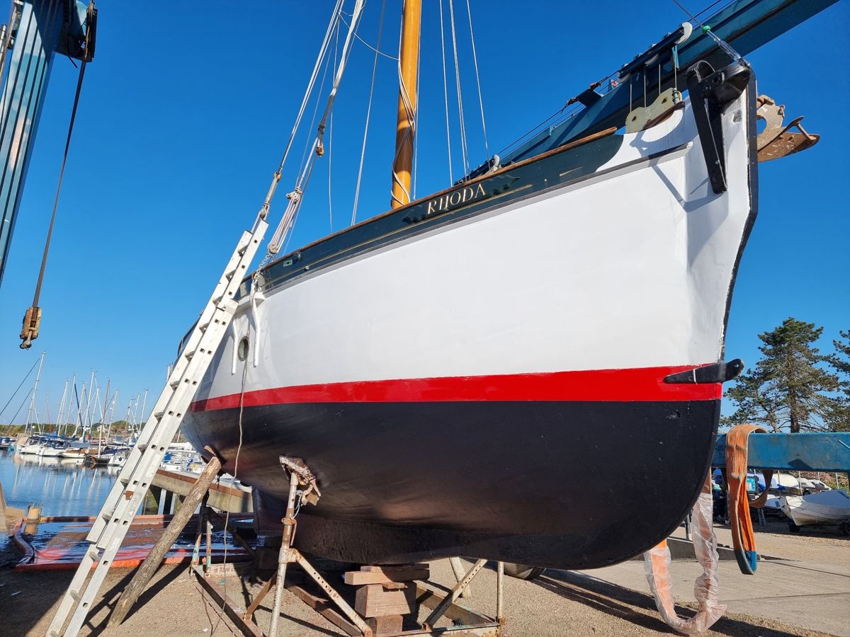 Rhoda ashore in the hoist with white topsides, red boot-top and her new varnished mast stepped