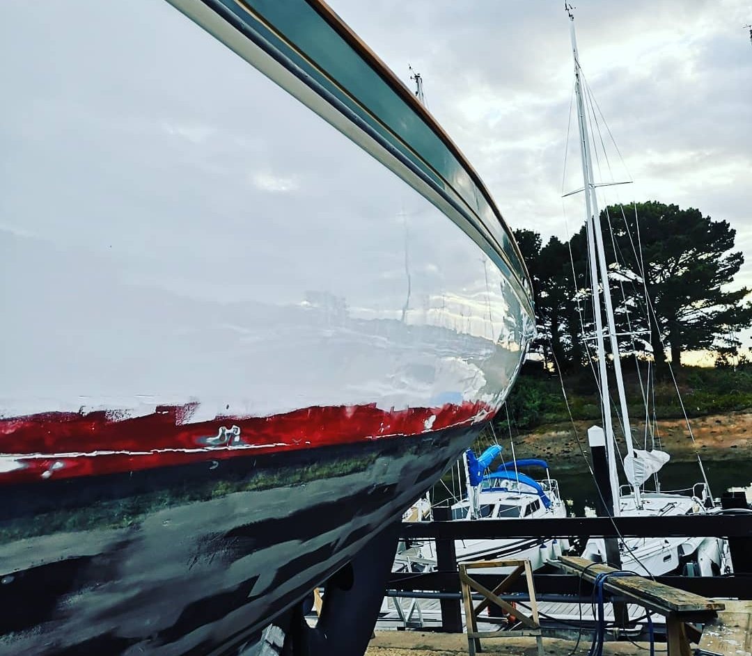 Rhoda's topsides after the first gloss topcoat, reflecting the sky, above an unfinished red boot-top