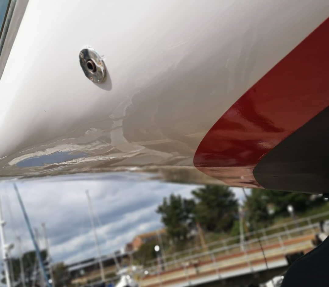 Close view of Rhoda's gloss topsides and red boot-top, the harbour reflected in the paint