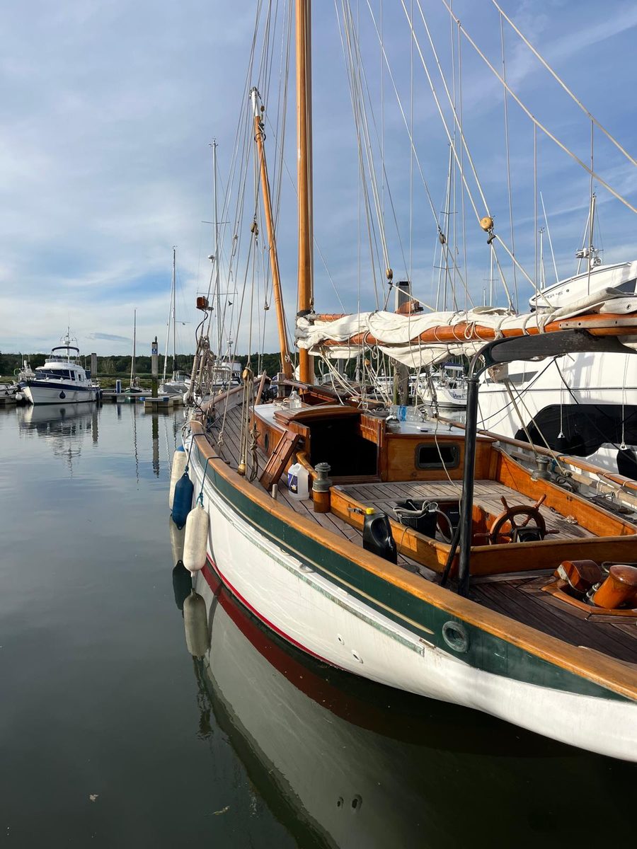 Rhoda alongside a marina pontoon, varnished brightwork and white topsides reflected in still water