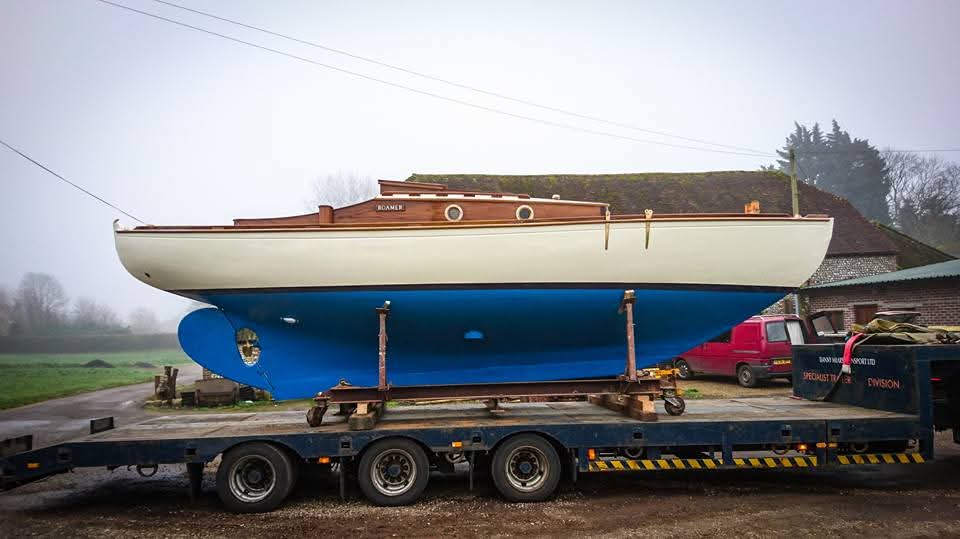 Roamer after restoration: cream topsides, blue antifouling and varnished coachroof, loaded for transport