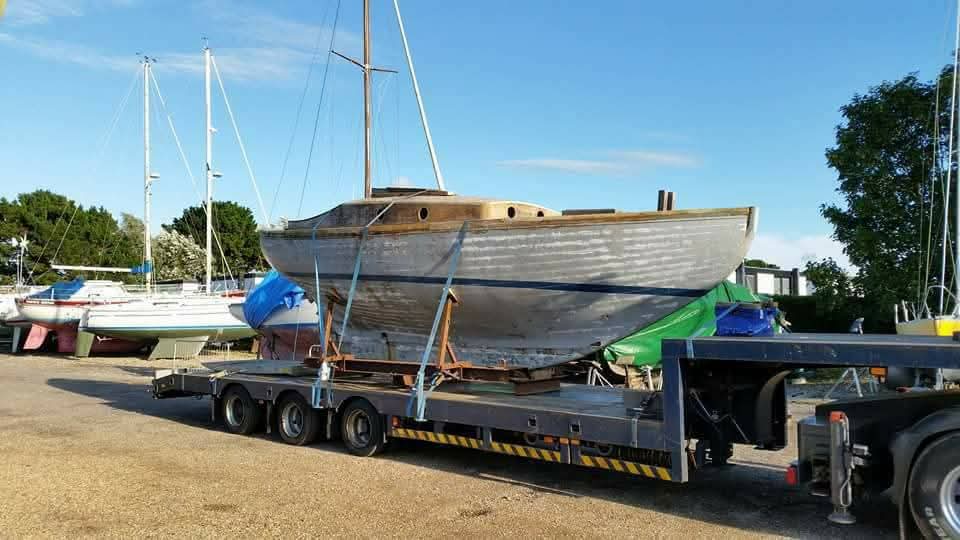 Roamer before restoration: bare grey weathered hull strapped to a low-loader trailer