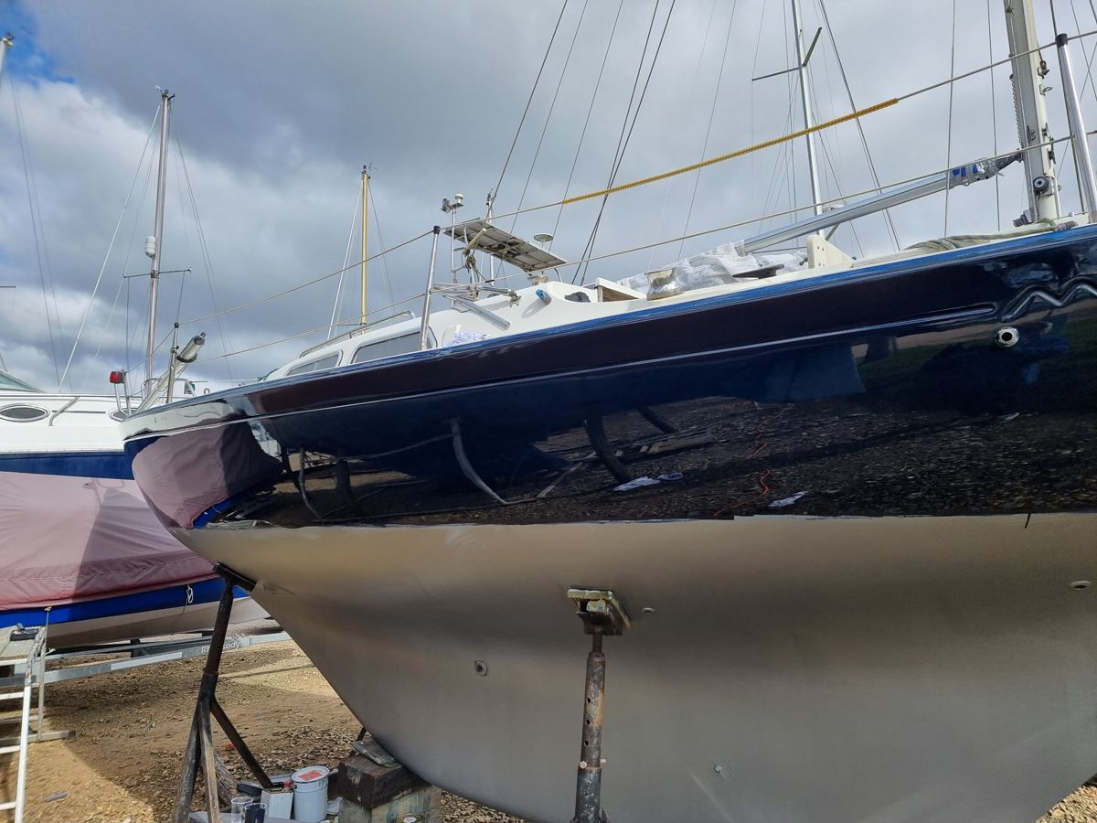 Sempre en Giro's navy topsides refinished to a mirror gloss, reflecting the boatyard