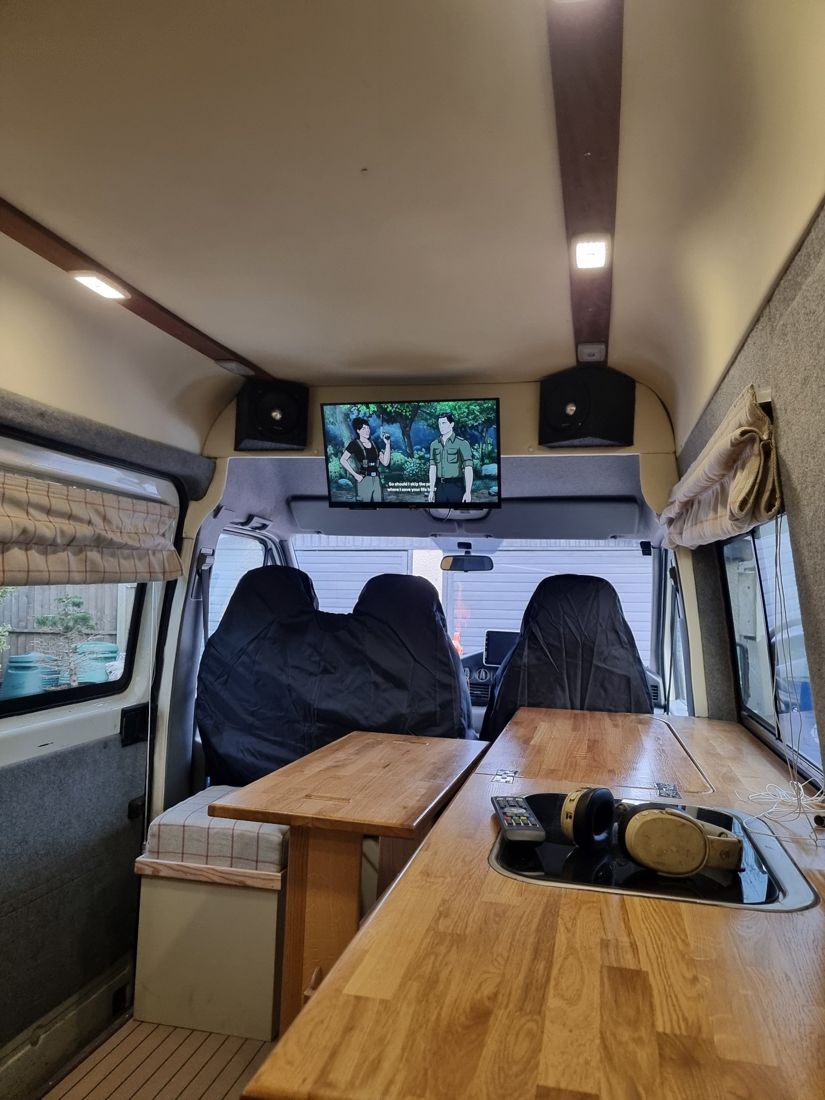 Van interior with lights on, showing timber ceiling battens, speakers and a screen above the cab